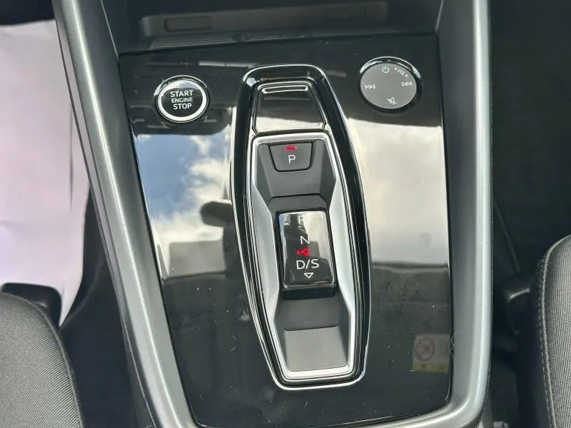 Gros plan sur la console centrale noire brillante de l'Audi A3 Sportback 2024 avec bouton start et levier de boîte auto.