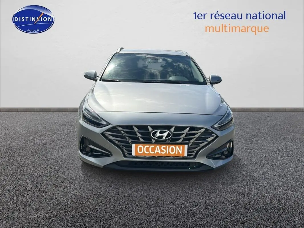 Vue frontale d'une Hyundai i30 SW gris clair avec calandre large et feux LED fins, en extérieur sur sol bitumé.