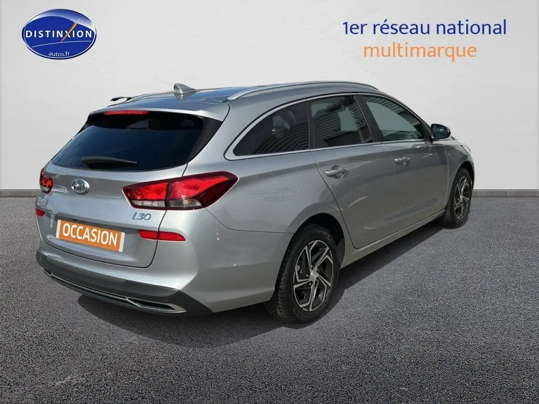 Vue 3/4 arrière droite d'une Hyundai i30 SW gris clair avec jantes alliage et vitres surteintées.