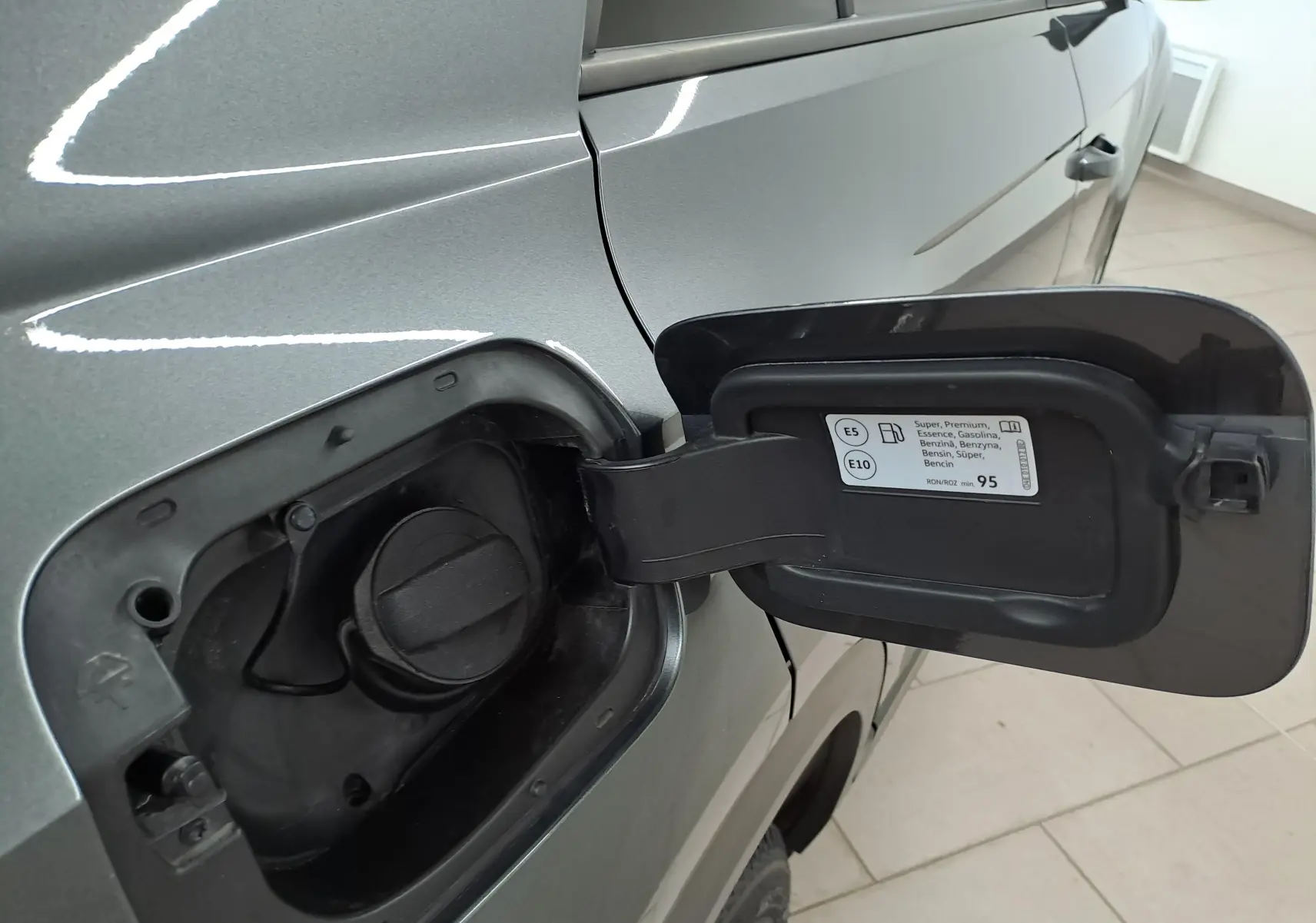 Détail de la trappe à carburant ouverte côté gauche du Volkswagen T-Roc gris Indium 2024 avec bouchon visible.