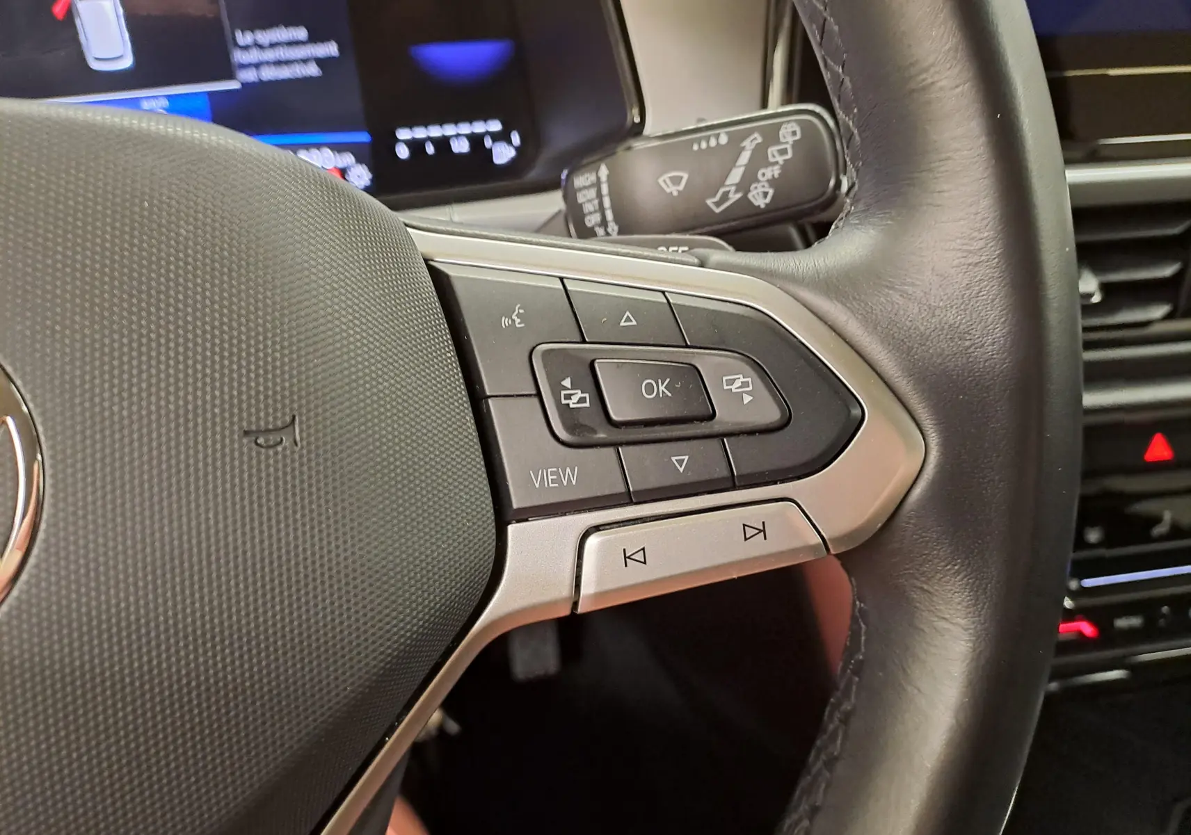 Gros plan sur les commandes à droite du volant en cuir du Volkswagen T-Roc 2024, avec boutons multifonctions et affichage numérique partiel.