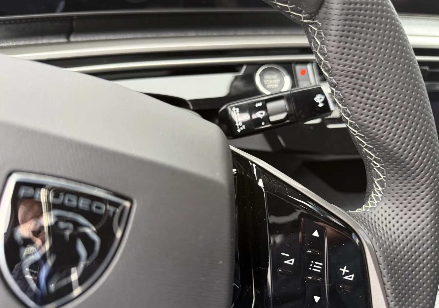Gros plan sur le volant noir perforé du Peugeot 3008 Hybrid 2025 avec commandes intégrées et logo au centre.