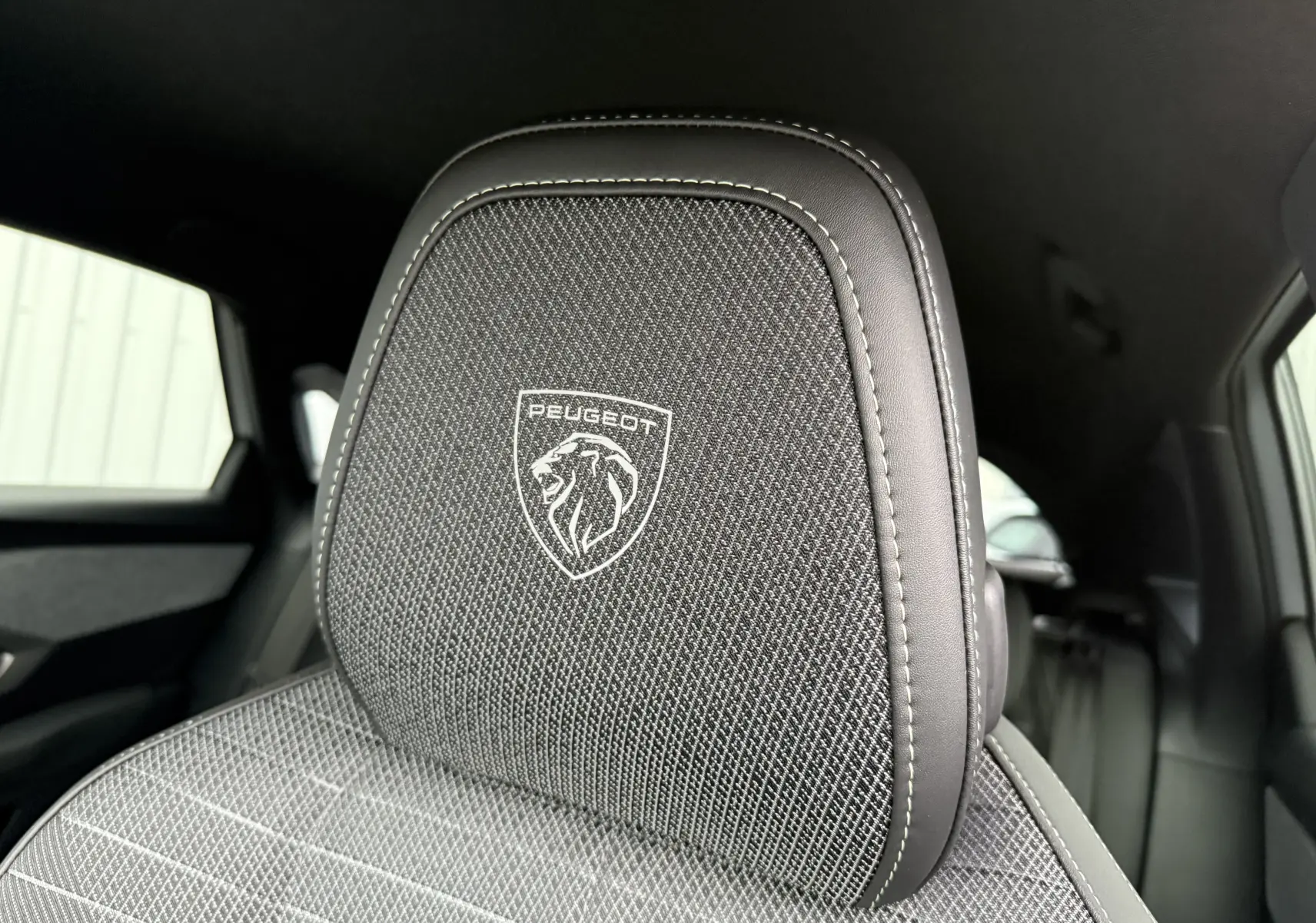 Gros plan sur l'appui-tête avant en tissu noir avec logo Peugeot brodé dans l'habitacle du 3008 hybride 2025.