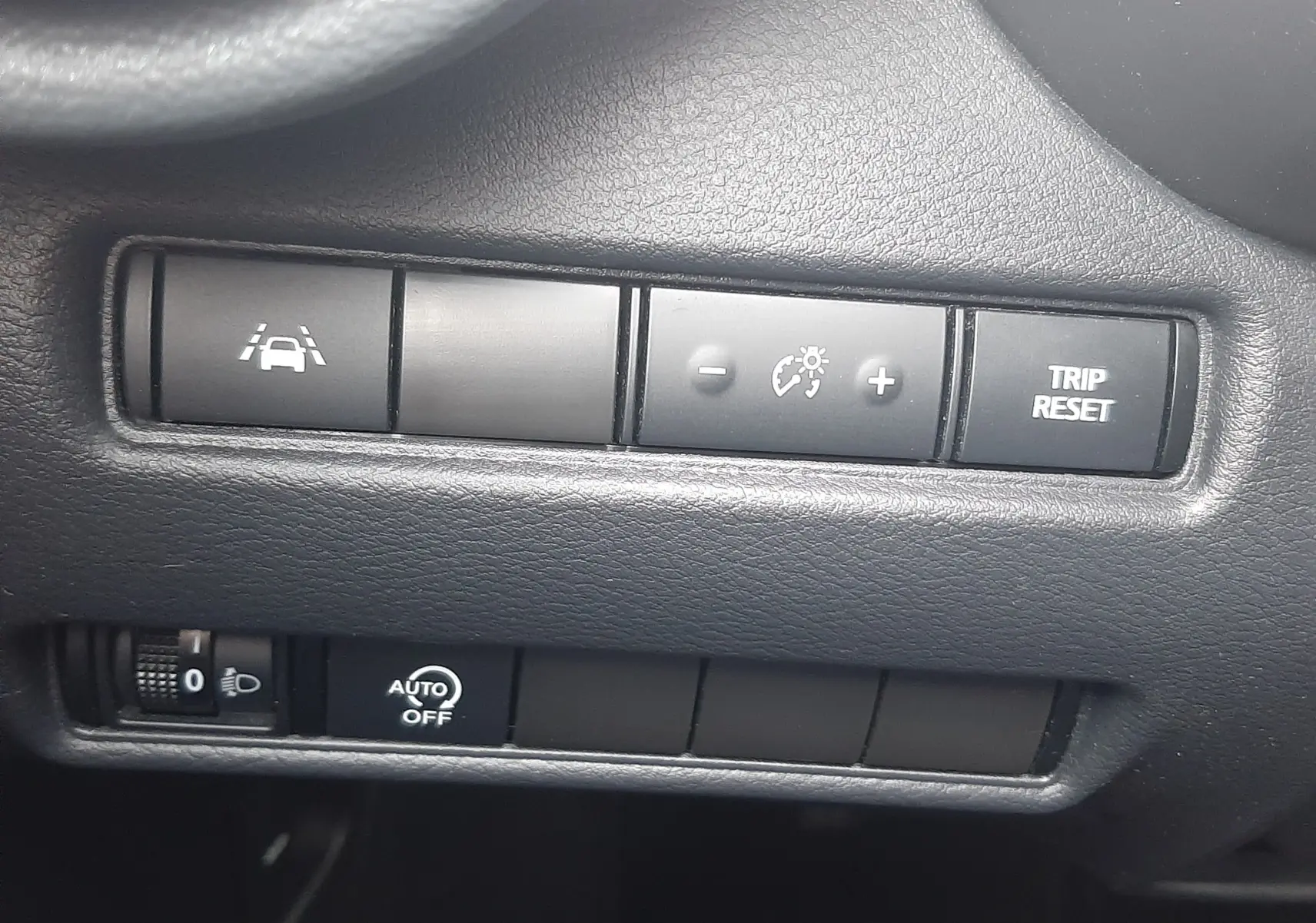 Gros plan sur les boutons de commande noirs du tableau de bord du Nissan Juke gris, avec régulateur de vitesse et reset compteur.