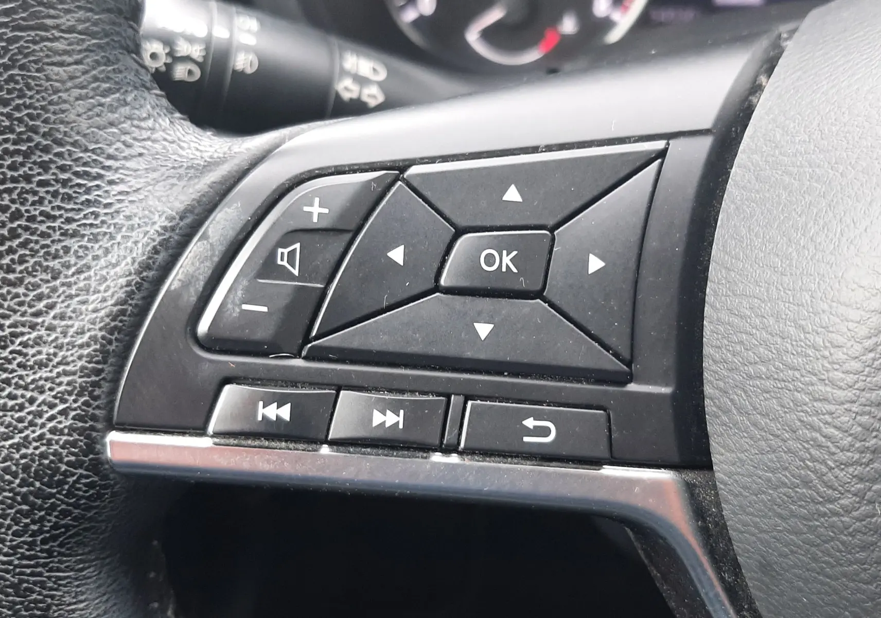 Gros plan sur les commandes noires du volant côté gauche du Nissan Juke gris 2020, avec tableau de bord flou en arrière-plan.