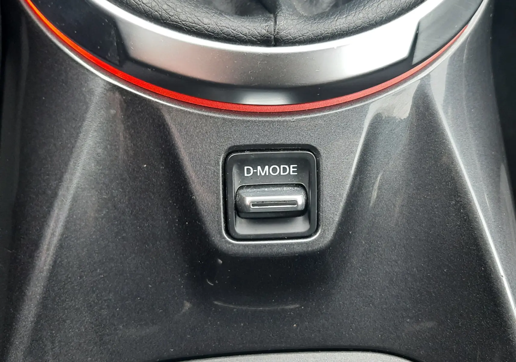 Gros plan sur le bouton D-MODE noir au centre de la console entre le levier de vitesse et le porte-gobelet du Nissan Juke gris.