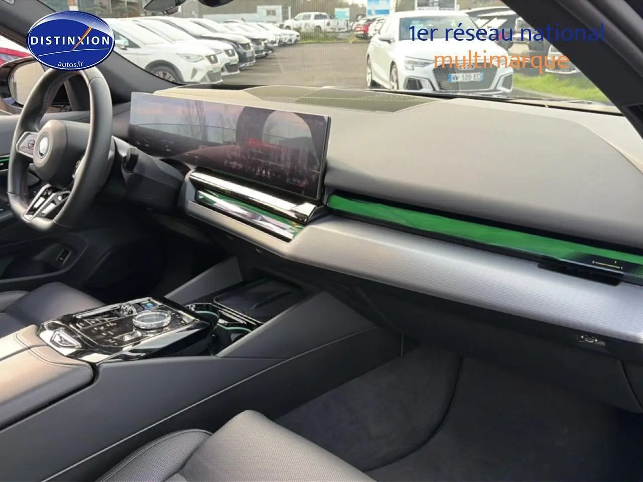 Intérieur BMW Série 5 i5 M60 2024 vu côté passager, tableau de bord moderne avec écran large et inserts verts.