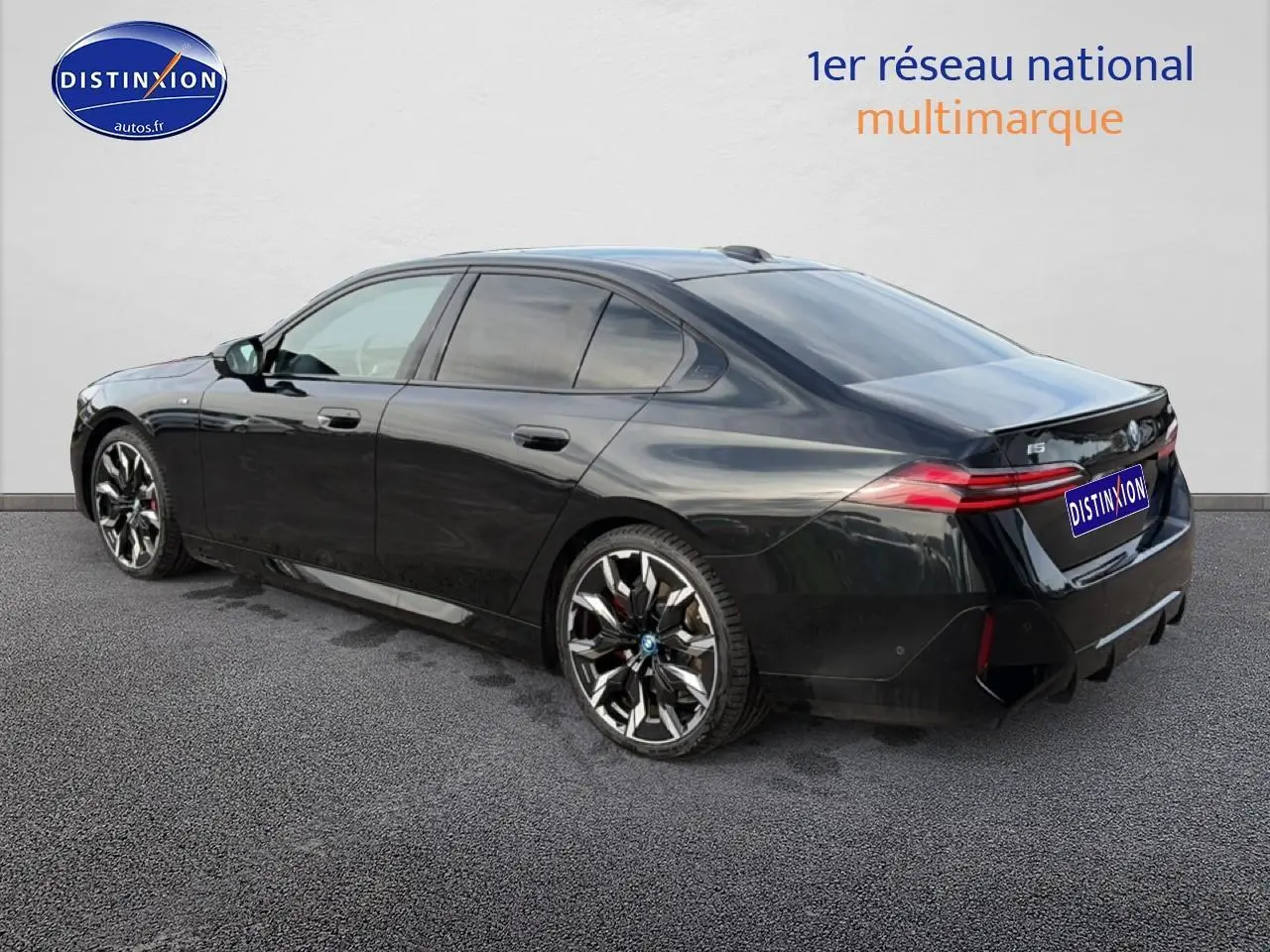 BMW Série 5 i5 M60 noire vue 3/4 arrière droit, avec jantes alu bicolores et feux arrière LED allumés.