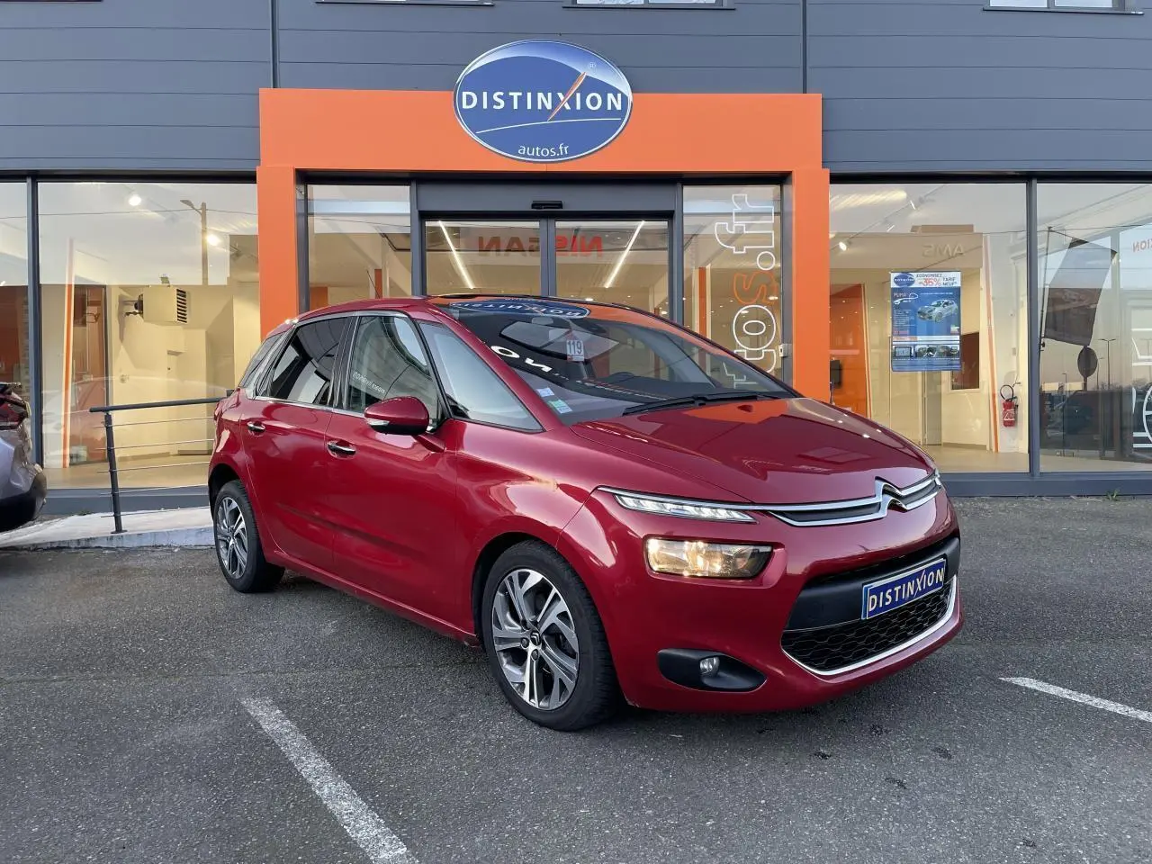 Citroën C4 Picasso rouge foncé vue 3/4 avant droit devant un showroom Distinxion.