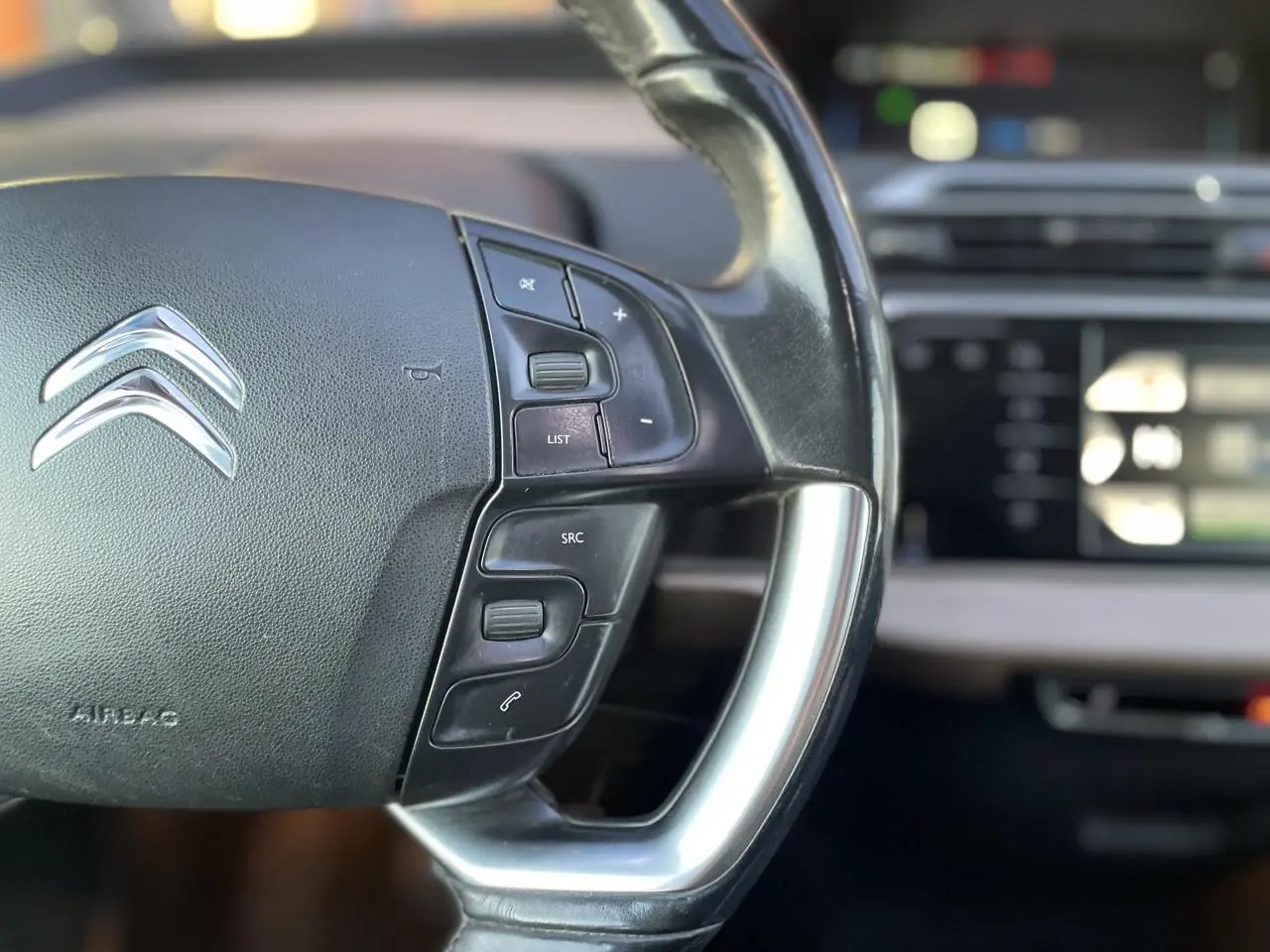 Gros plan sur le volant noir de la Citroën C4 Picasso 2014, avec commandes intégrées et logo chromé visible.