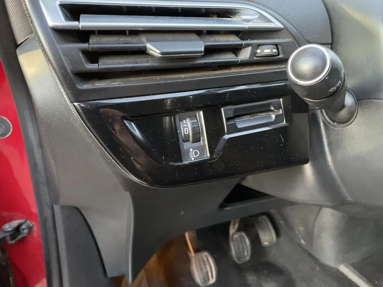 Détail intérieur côté conducteur montrant la commande des phares et la pédale d'embrayage d'une Citroën C4 Picasso rouge foncé.