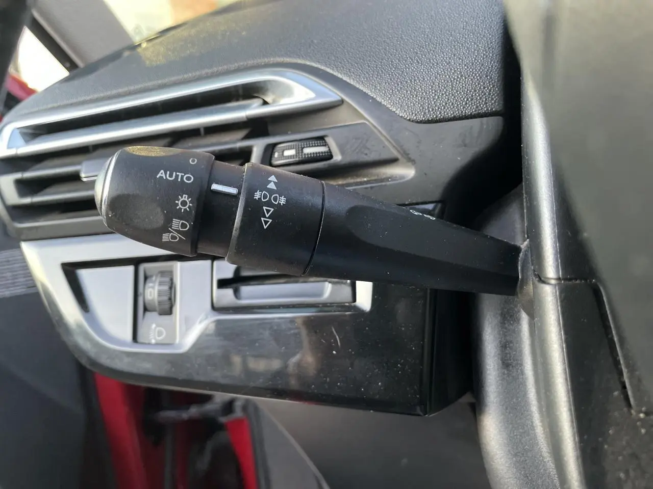 Gros plan sur la commande des phares et antibrouillard à gauche du volant d'un Citroën C4 Picasso rouge foncé.