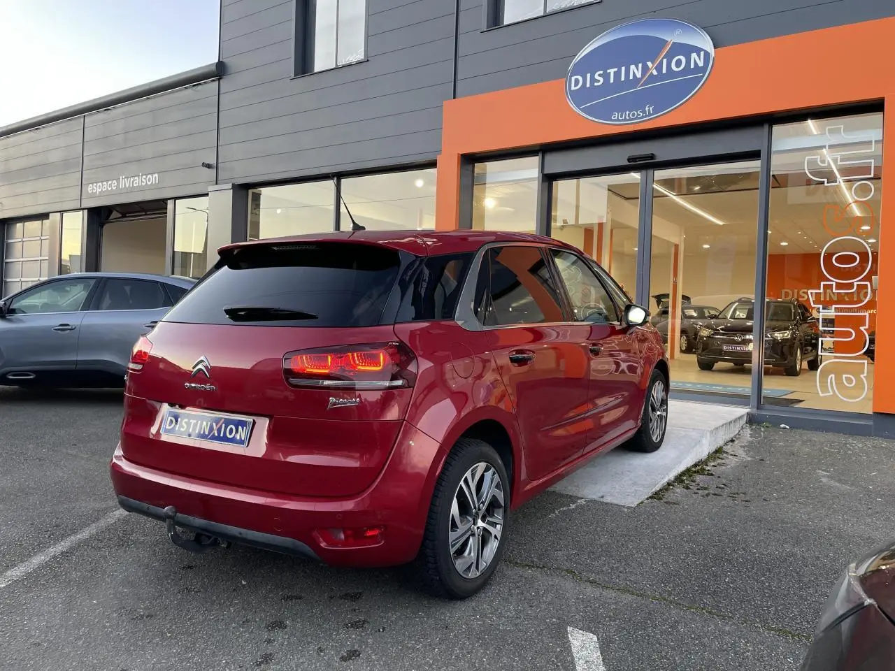 Vue 3/4 arrière droite d'une Citroën C4 Picasso rouge foncé stationnée devant un showroom Distinxion.