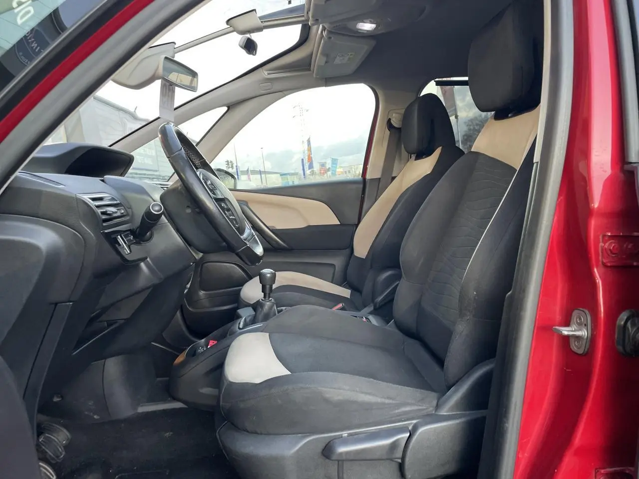 Intérieur avant du Citroën C4 Picasso rouge foncé 2014, sièges bicolores noirs et beige, volant et levier de vitesse manuelle visibles.
