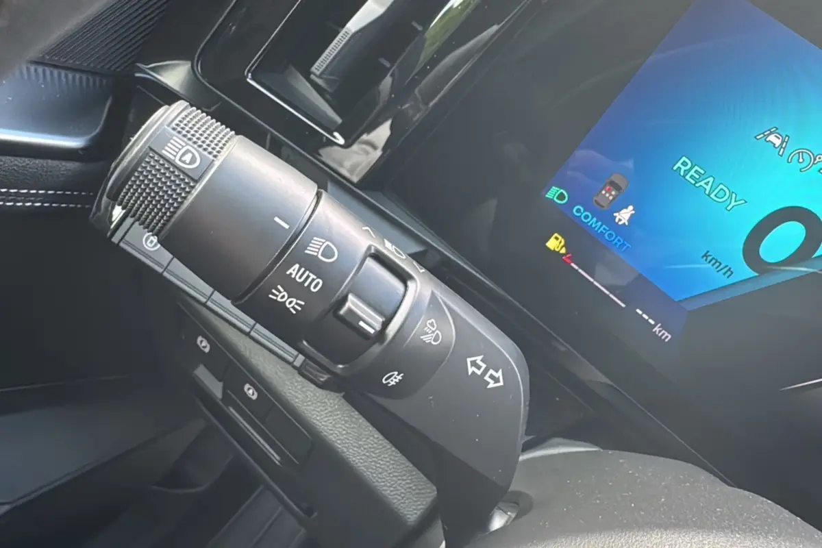 Gros plan sur la commande des phares et clignotants du Renault Austral E-TECH 200 bleu iron avec tableau de bord digital allumé.