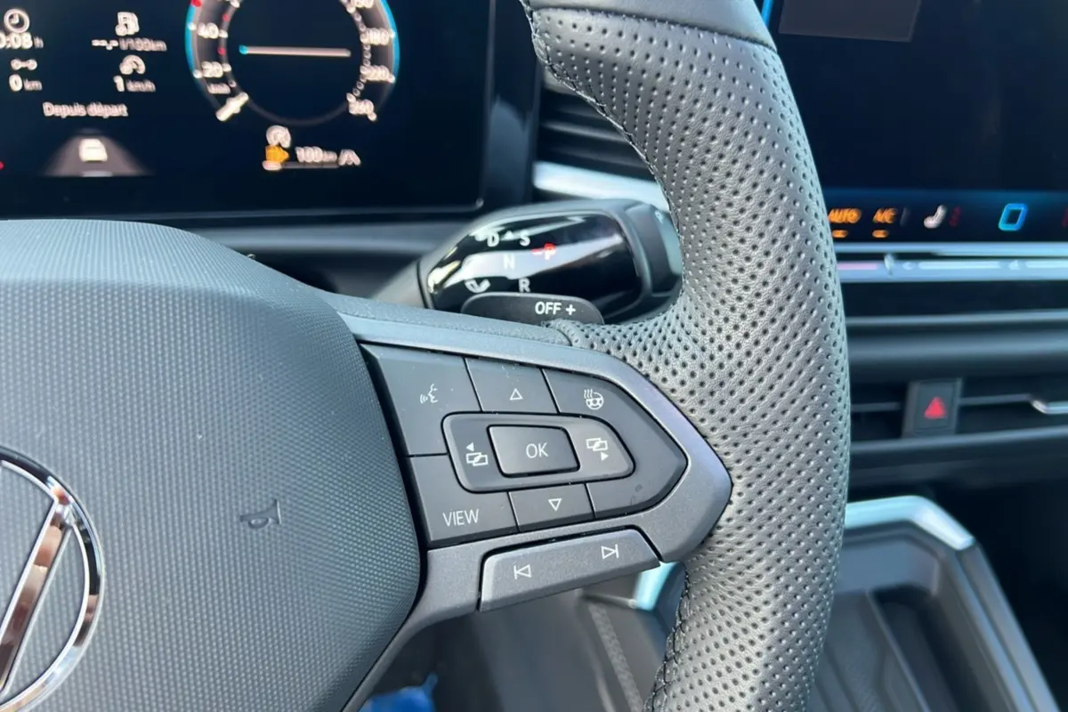 Gros plan sur le volant cuir perforé côté droit du Volkswagen T-Roc gris loup avec commandes multifonctions et tableau de bord numérique.