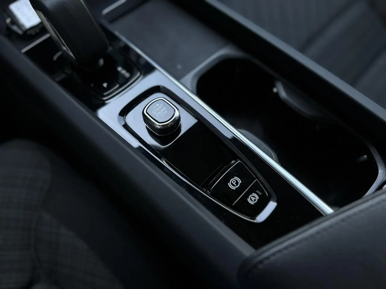 Gros plan sur la console centrale noire brillante du Volvo S60 B4 197 DCT7 MHEV Core+ avec bouton start/stop et frein électronique.