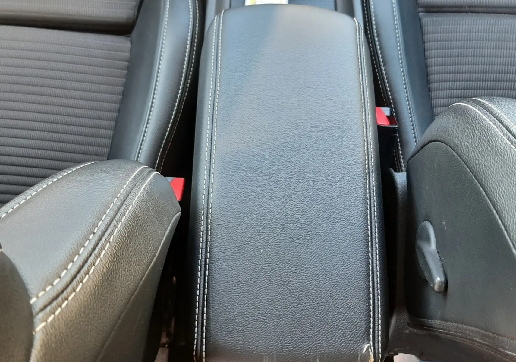 Vue rapprochée de l'accoudoir central en cuir noir avec surpiqûres blanches entre les sièges avant d'un Renault Scenic IV.
