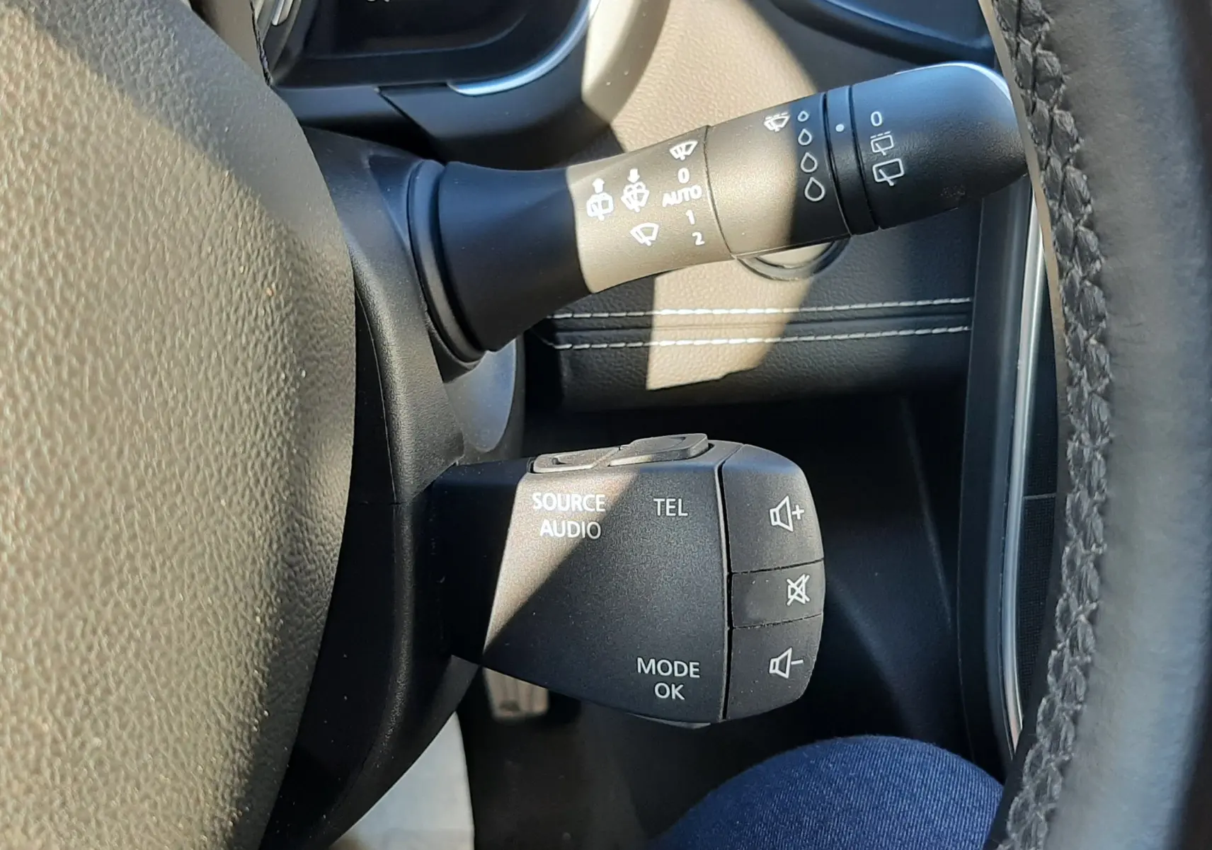 Gros plan sur les commandes audio et essuie-glace à gauche du volant du Renault Scenic IV blanc nacré avec intérieur noir.