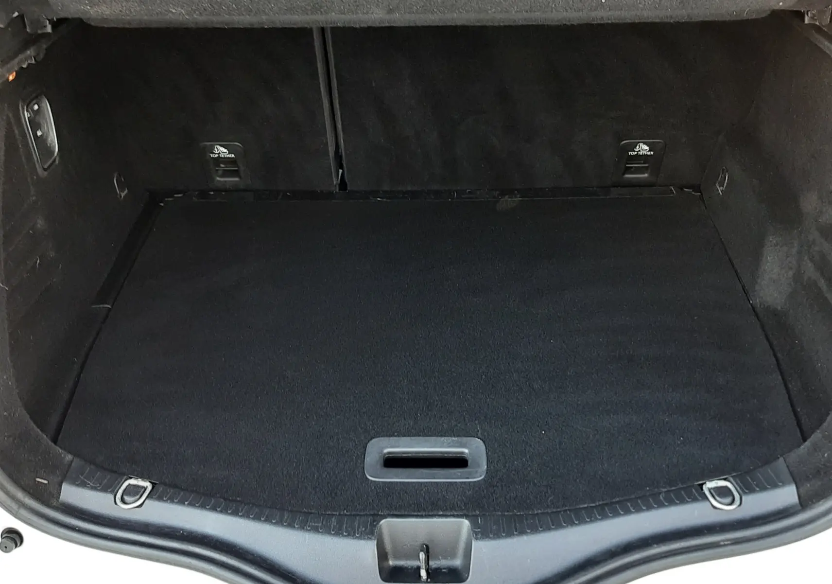 Coffre ouvert vu de l'arrière d'un Renault Scénic IV blanc nacré, intérieur noir et tapis de coffre propre.