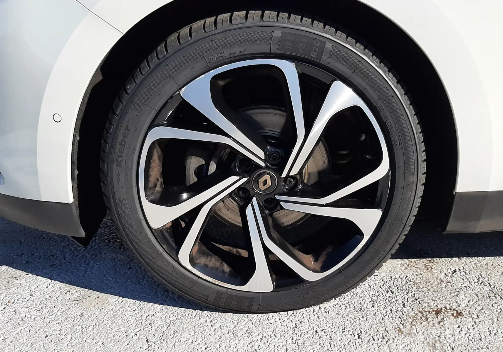 Gros plan sur la roue avant gauche blanche nacrée du Renault Scénic IV avec jante noire et argentée au design moderne.