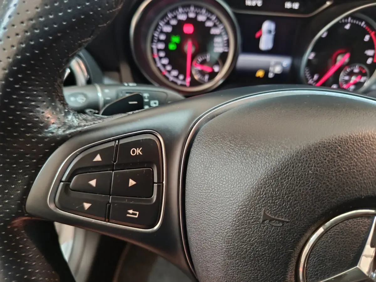 Gros plan sur le volant cuir noir de la Mercedes GLA 200 d, avec commandes multifonctions et tableau de bord en arrière-plan.