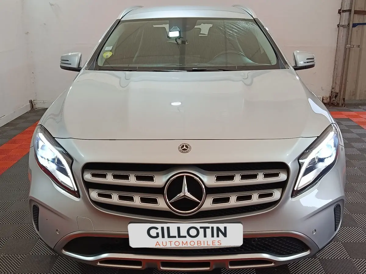 Vue frontale d’un Mercedes GLA 200 d Business Executive gris clair avec phares LED allumés en intérieur showroom.