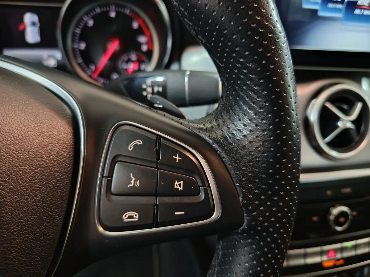 Gros plan sur la partie gauche du volant cuir perforé d’un Mercedes GLA 200 d gris clair, avec commandes audio intégrées.