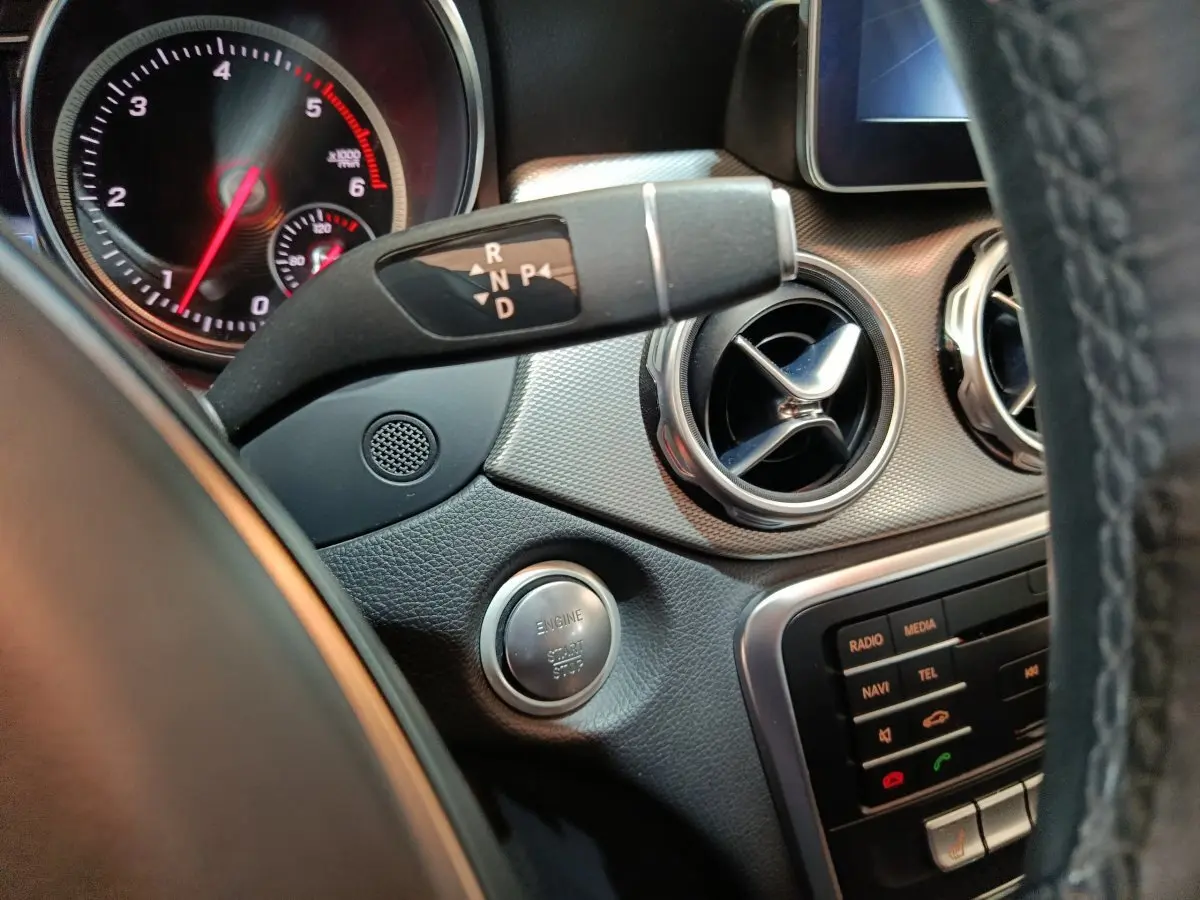 Vue rapprochée de la console centrale et du levier de vitesses d'une Mercedes GLA 200 d gris clair, avec bouton démarrage et aérateurs ronds.