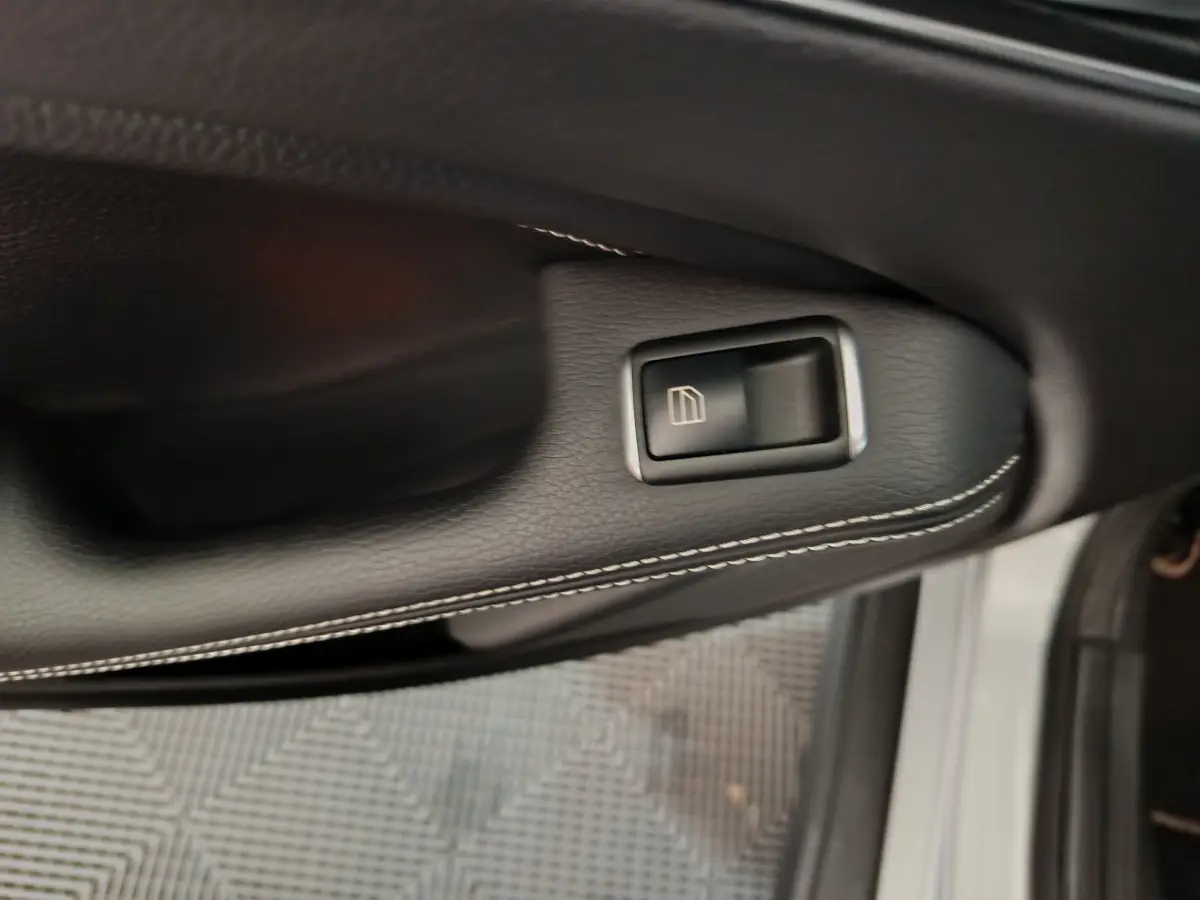 Gros plan sur la commande de lève-vitre côté conducteur d'un Mercedes GLA 200 d gris clair, intérieur cuir noir.