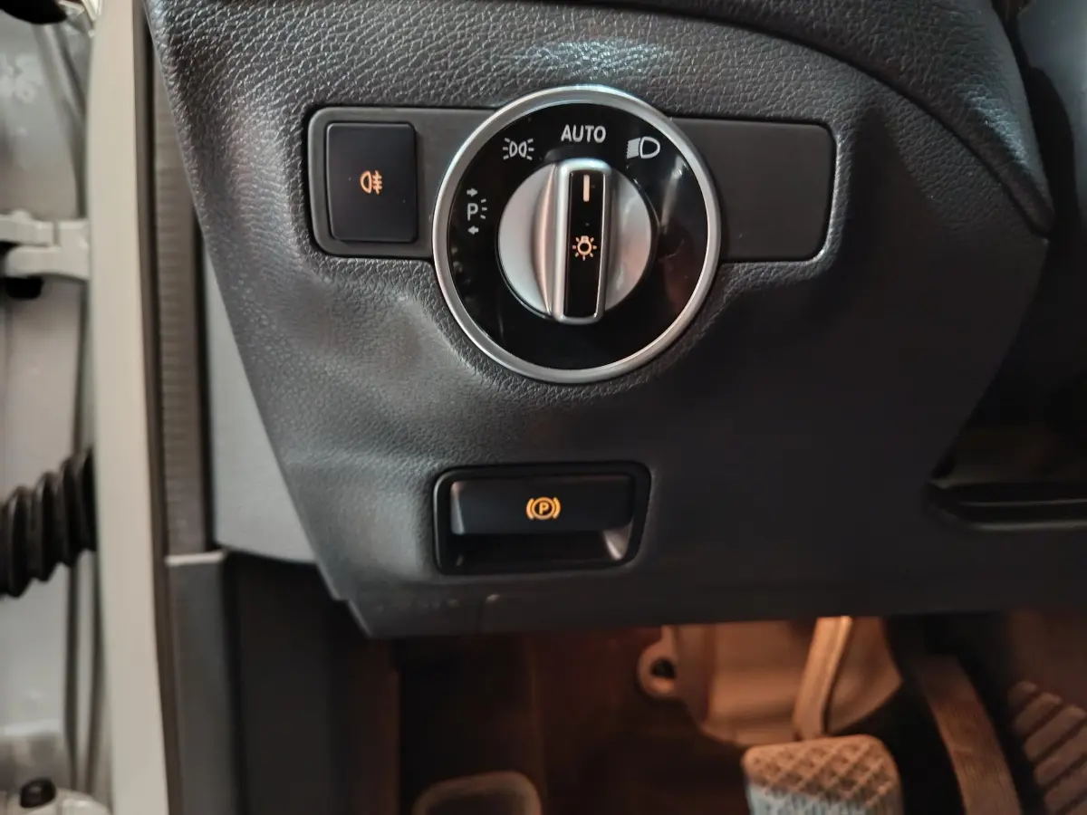 Gros plan sur le bouton des phares et frein à main électrique côté gauche d’un Mercedes GLA 200 d gris clair de 2018.