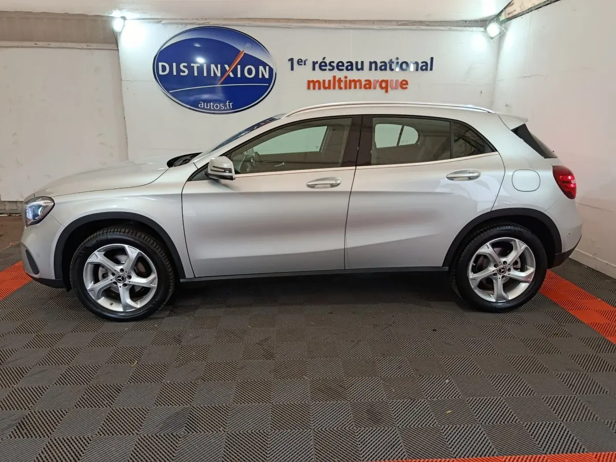 Profil droit d'un Mercedes GLA 200 d Business Executive gris clair, avec jantes alliage et rétroviseurs électriques, en intérieur showroom.