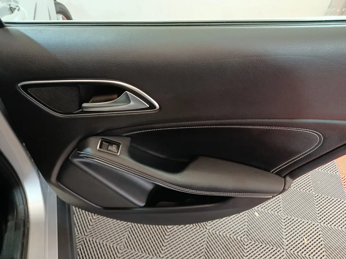 Gros plan sur la porte intérieure côté gauche d'une Mercedes GLA 200 d Business Executive gris clair, avec garniture cuir noire et surpiqûres blanches.