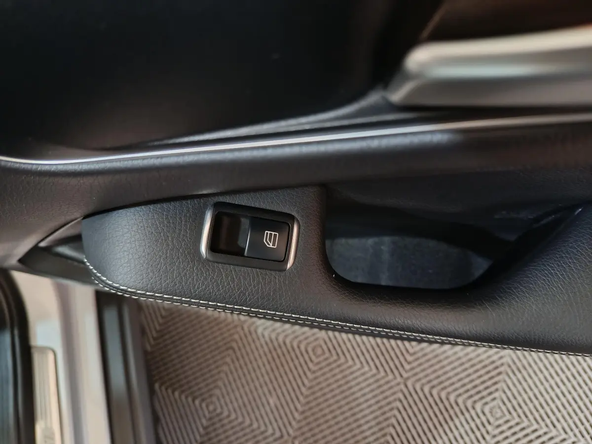 Gros plan sur la commande de lève-vitre côté conducteur en cuir noir avec surpiqûres dans un Mercedes GLA 200 d gris clair.