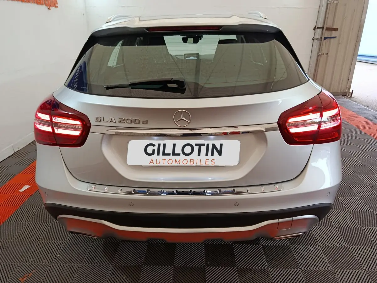 Vue arrière d'une Mercedes GLA 200 d gris clair avec feux LED allumés et logo central visible sur coffre.