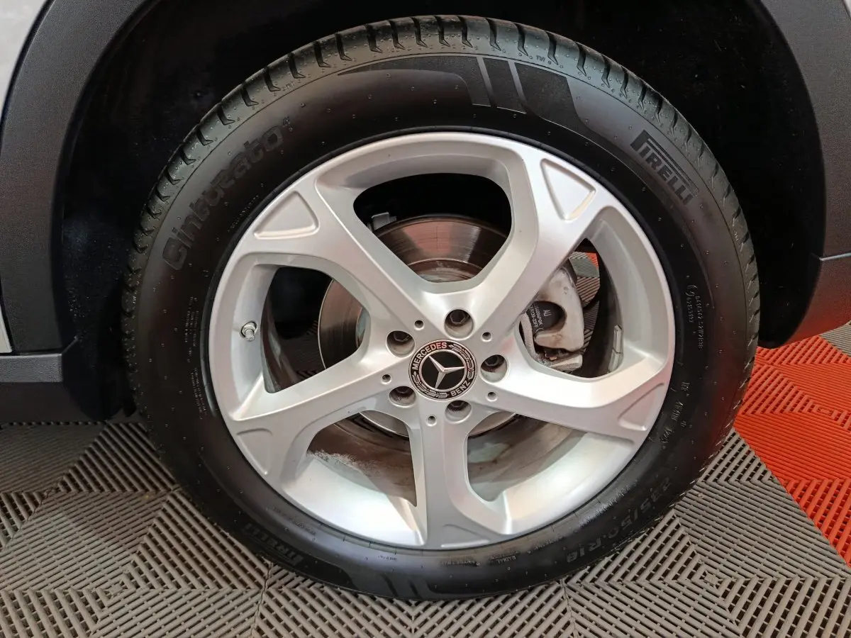 Gros plan sur la roue arrière droite d'un Mercedes GLA 200 d gris clair, avec partie de la carrosserie visible sur fond de sol texturé.