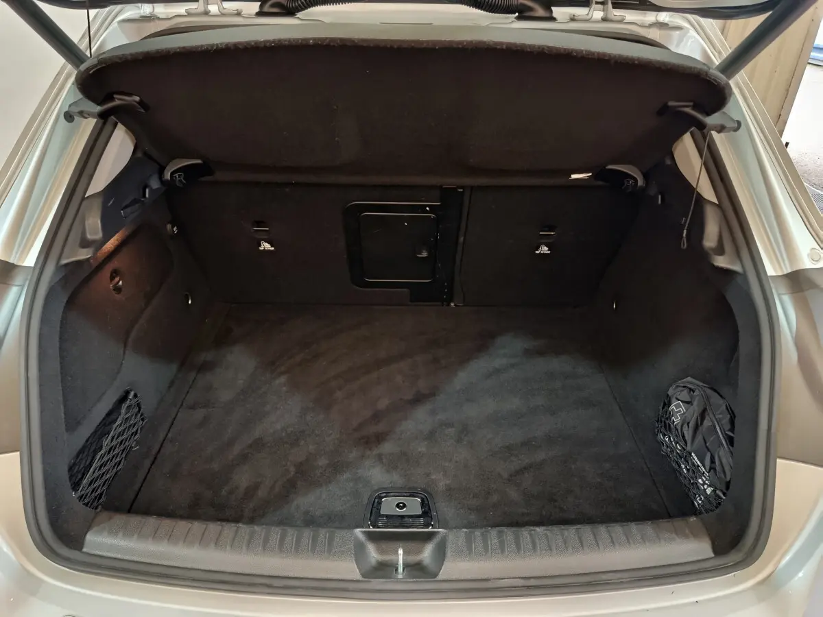 Coffre ouvert vu de l'arrière d'un Mercedes GLA 200 d gris clair, avec tapis noir et filet de rangement latéral.