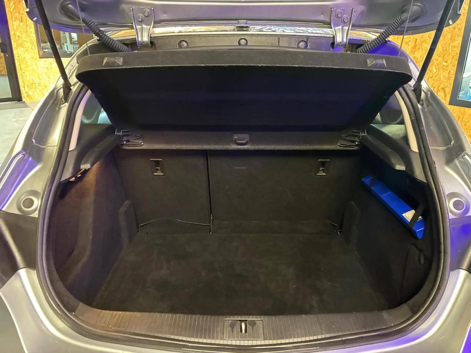 Coffre ouvert d'une Opel Astra gris 2015, vue arrière montrant l'espace de chargement vide et la tablette arrière relevée.