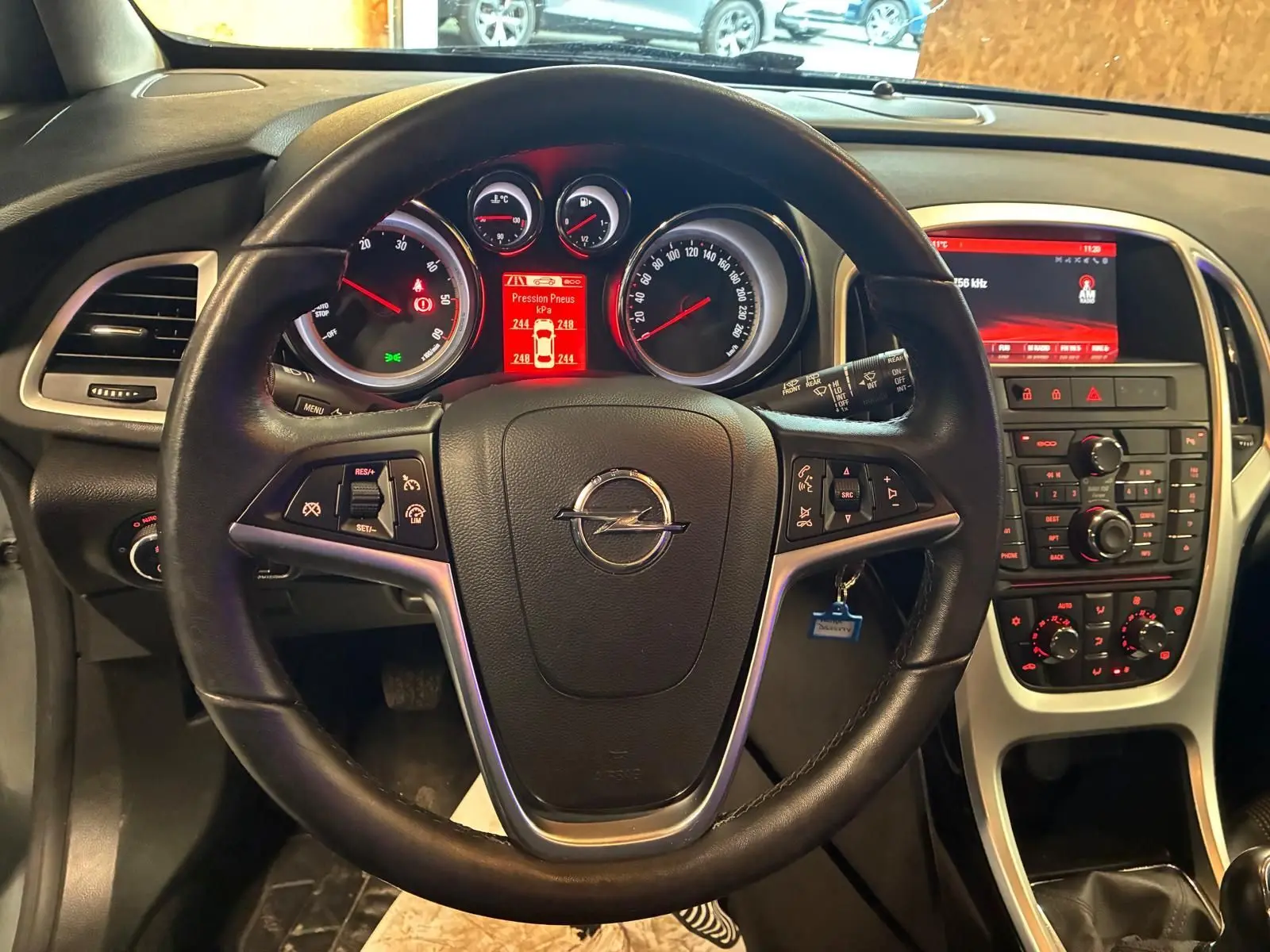 Vue intérieure centrée sur le volant noir d'une Opel Astra 2015 avec tableau de bord et console centrale rétroéclairés en rouge.