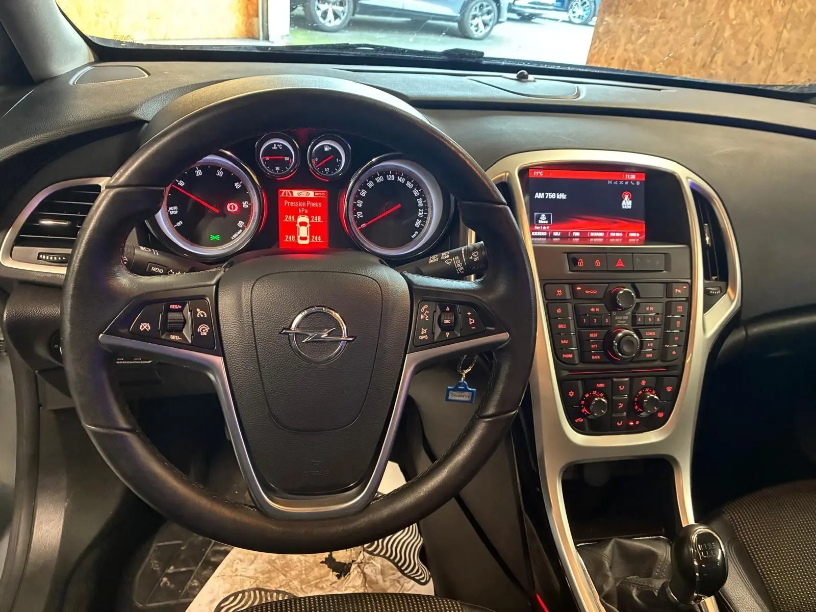 Vue intérieure centrée sur le volant et le tableau de bord de l'Opel Astra gris, avec écran central et levier de vitesse manuel.