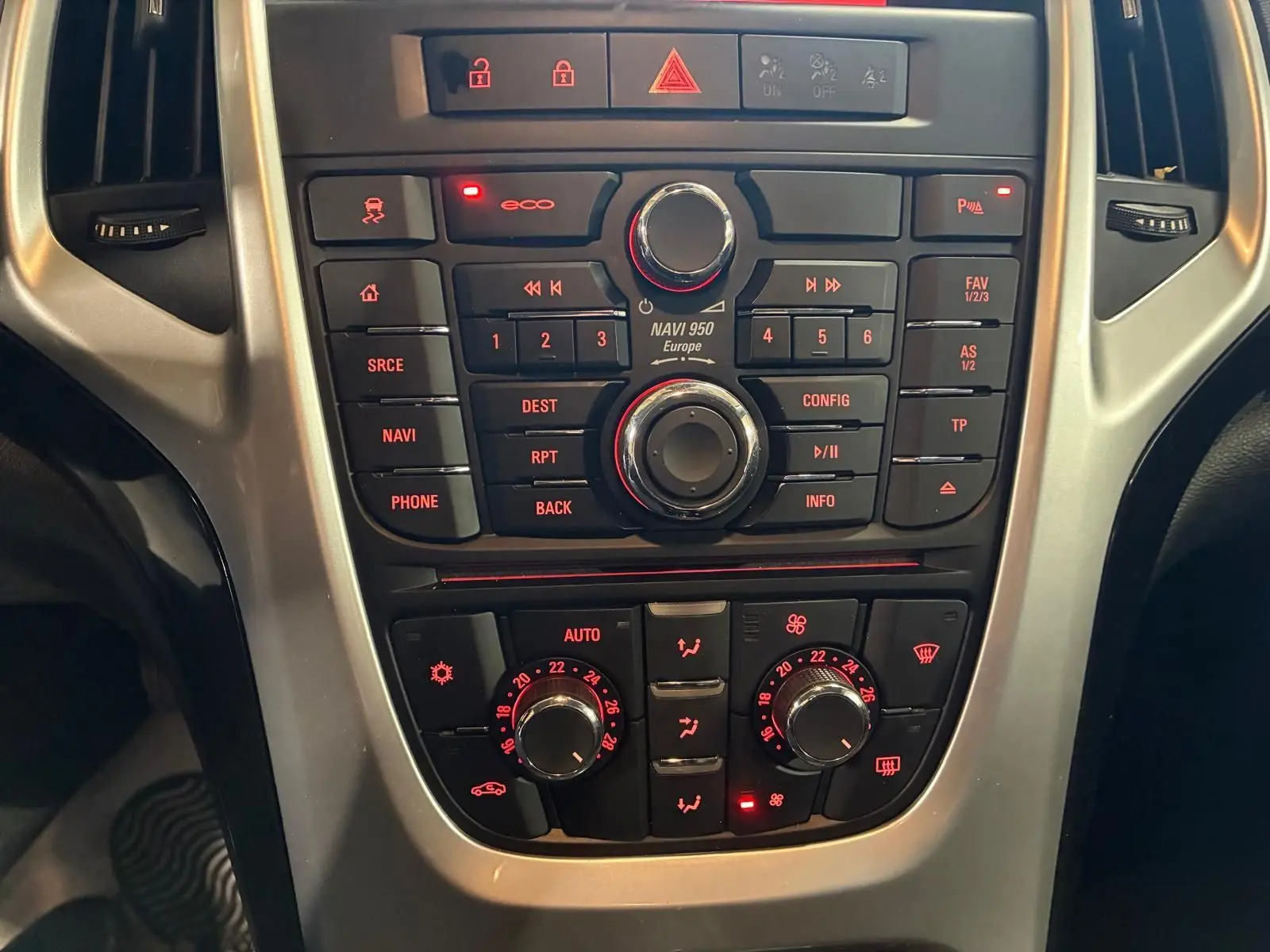 Vue rapprochée du tableau de bord de l'Opel Astra 1.6 CDTI 110 gris, avec commandes de navigation et climatisation éclairées.