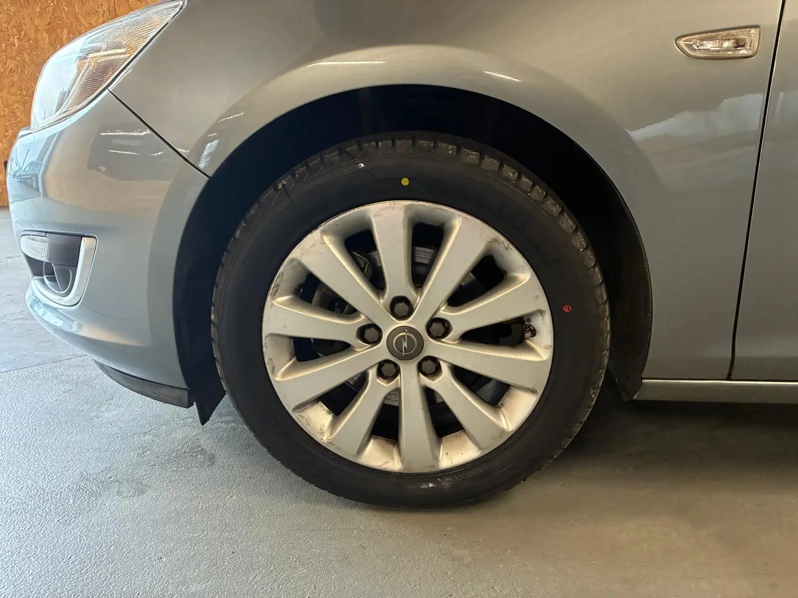 Gros plan sur la roue avant gauche d'une Opel Astra gris métallisé de 2015 avec jante alliage et clignotant latéral.