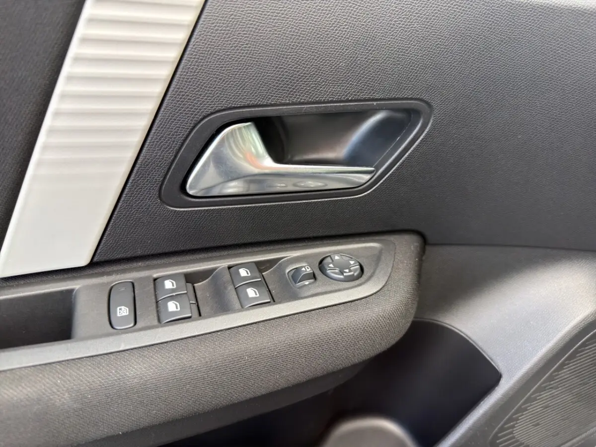 Gros plan sur la poignée intérieure et les commandes des vitres côté conducteur d'une Citroën C4 hybride gris foncé.