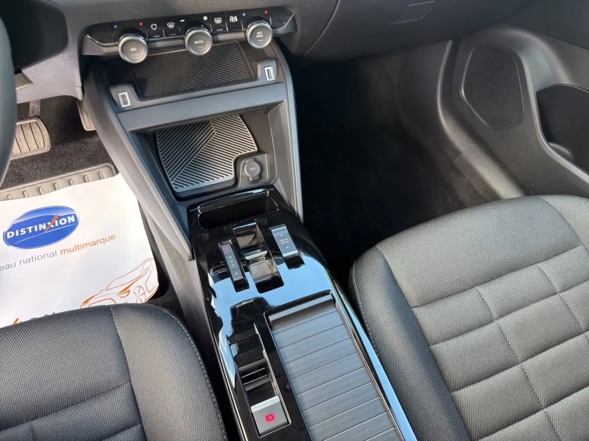 Vue intérieure centrée sur la console centrale noire brillante et les sièges tissu gris foncé du Citroën C4 hybride 2025.