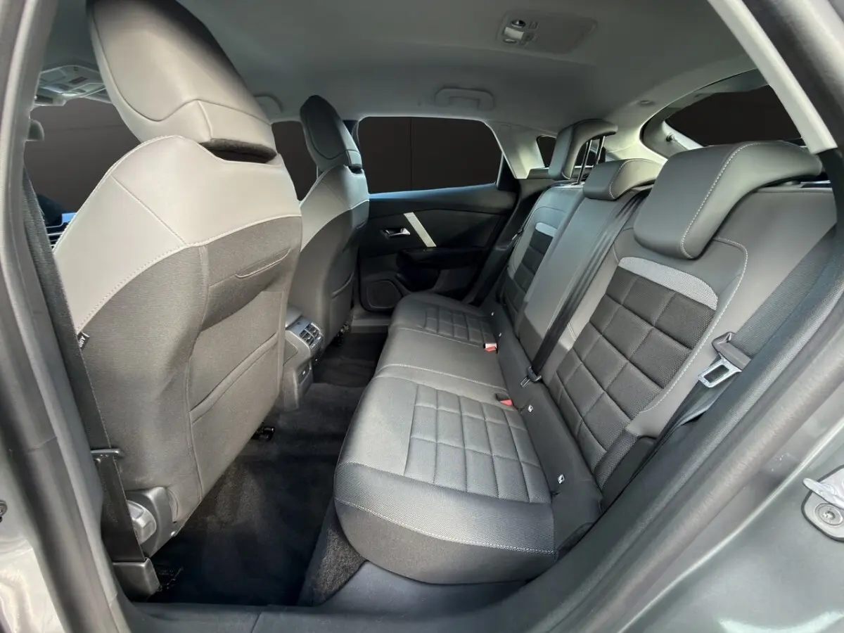 Vue intérieure arrière droite de la Citroën C4 hybride 2025, sièges tissu gris foncé avec appuie-têtes intégrés.