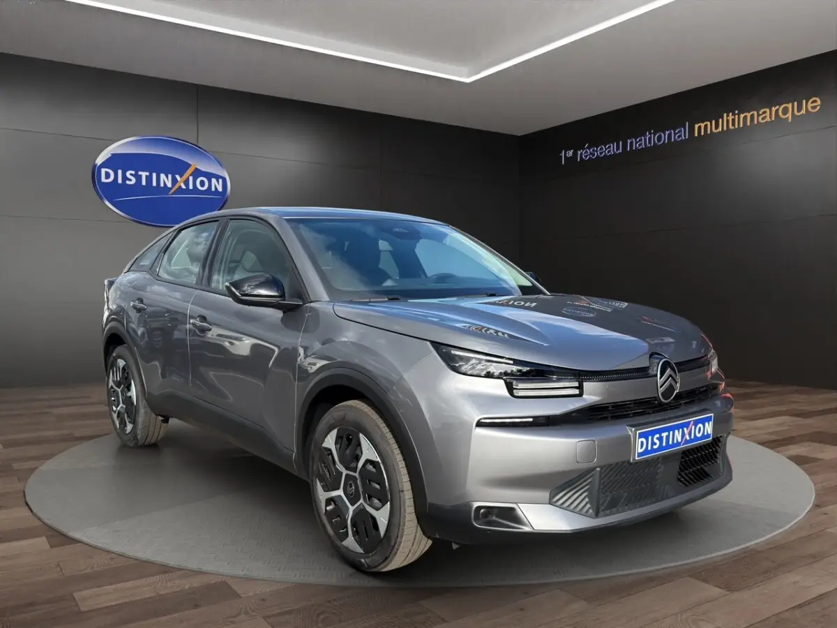 Citroën C4 hybride gris foncé vue 3/4 avant avec phares LED et jantes spécifiques en exposition showroom.