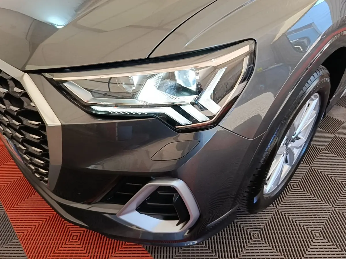 Gros plan sur l'avant droit gris clair de l'Audi Q3 Sportback 45 TFSI e avec phare LED et jante visible.