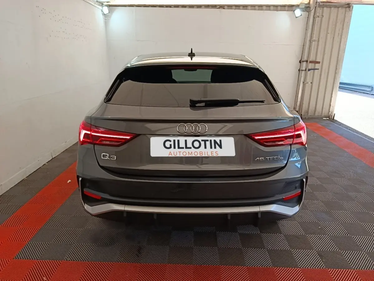 Vue arrière d'un Audi Q3 Sportback gris clair 45 TFSI e avec feux LED allumés dans un garage.