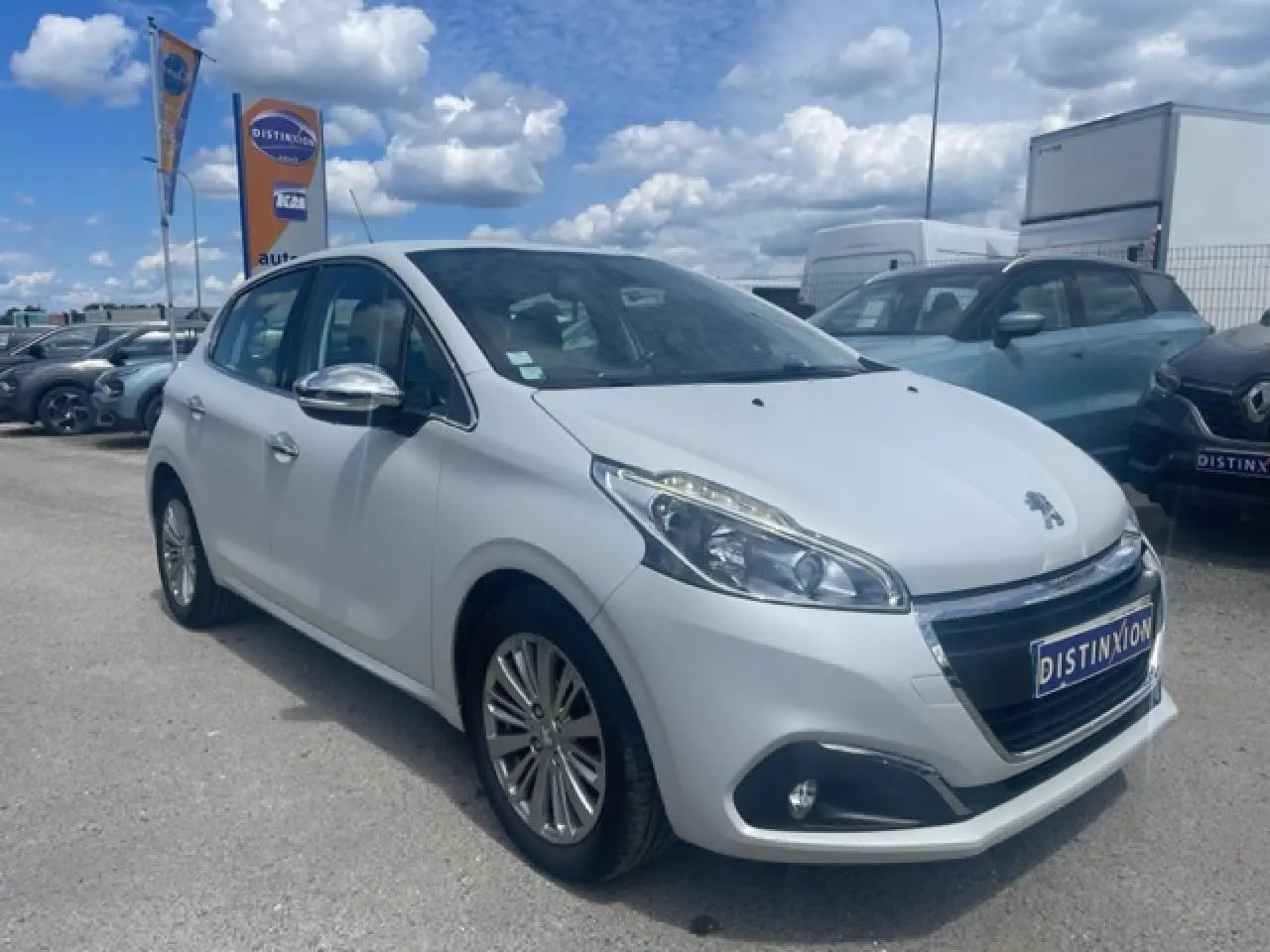 Peugeot 208 blanc perle en 3/4 avant droit avec jantes alliage et rétroviseurs chromés sur parking.
