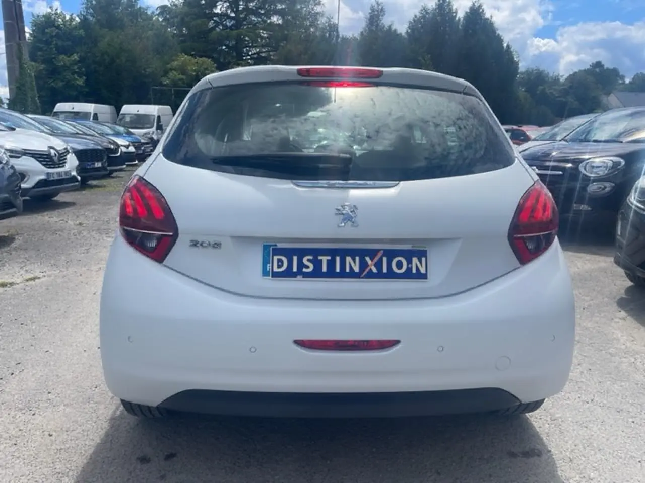 Vue arrière d'une Peugeot 208 blanche perle avec feux arrière rouges et plaque Distinxion visible.